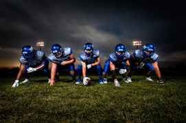 football players in blue jersey lined under grey white cloudy sky during sunset